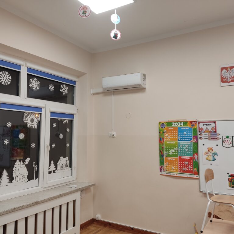 Widok na klimatyzator zamontowany wysoko na ścianie, pod sufitem.